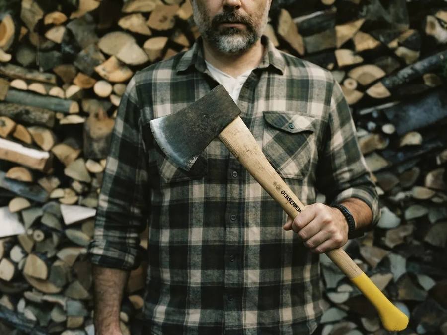 Mann mit Axt vor einem Holzstapel